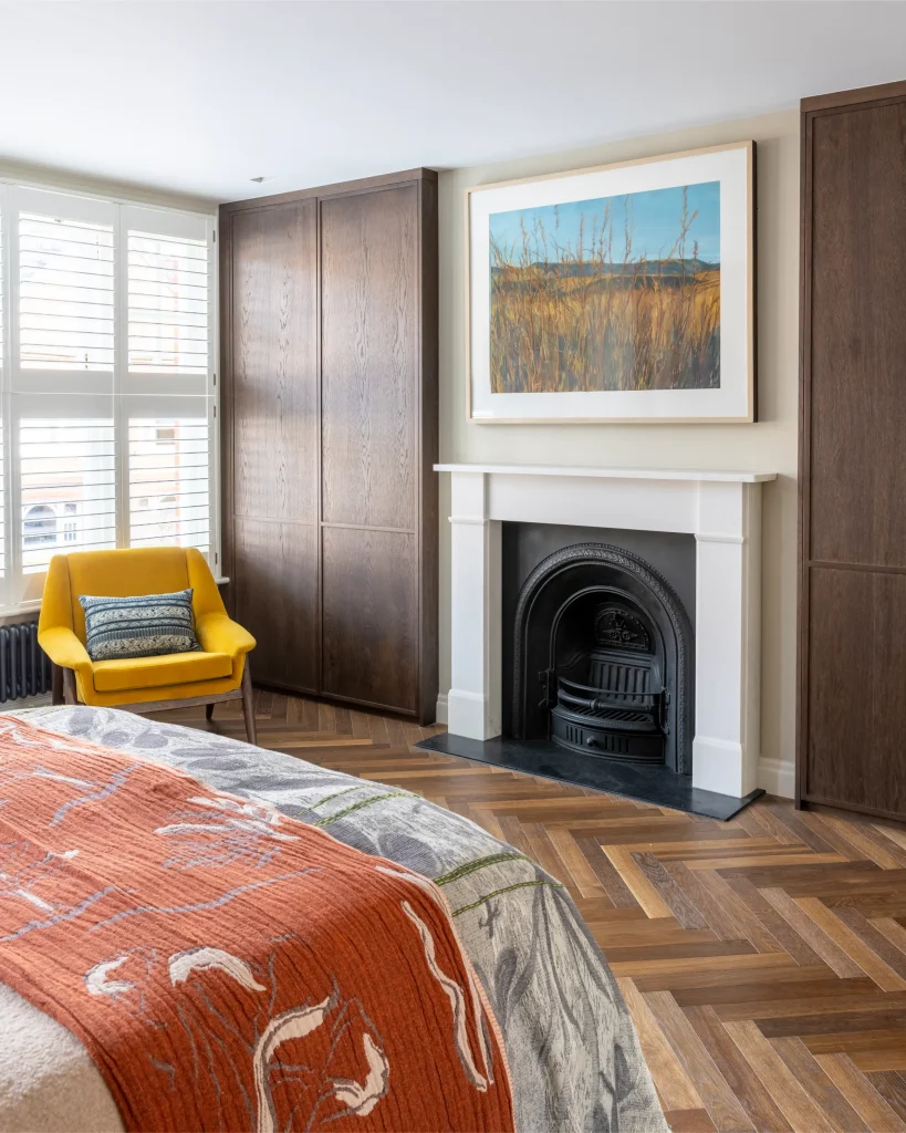 Modern London bedroom with fitted cabinetry, feature fireplace and parquet flooring design
