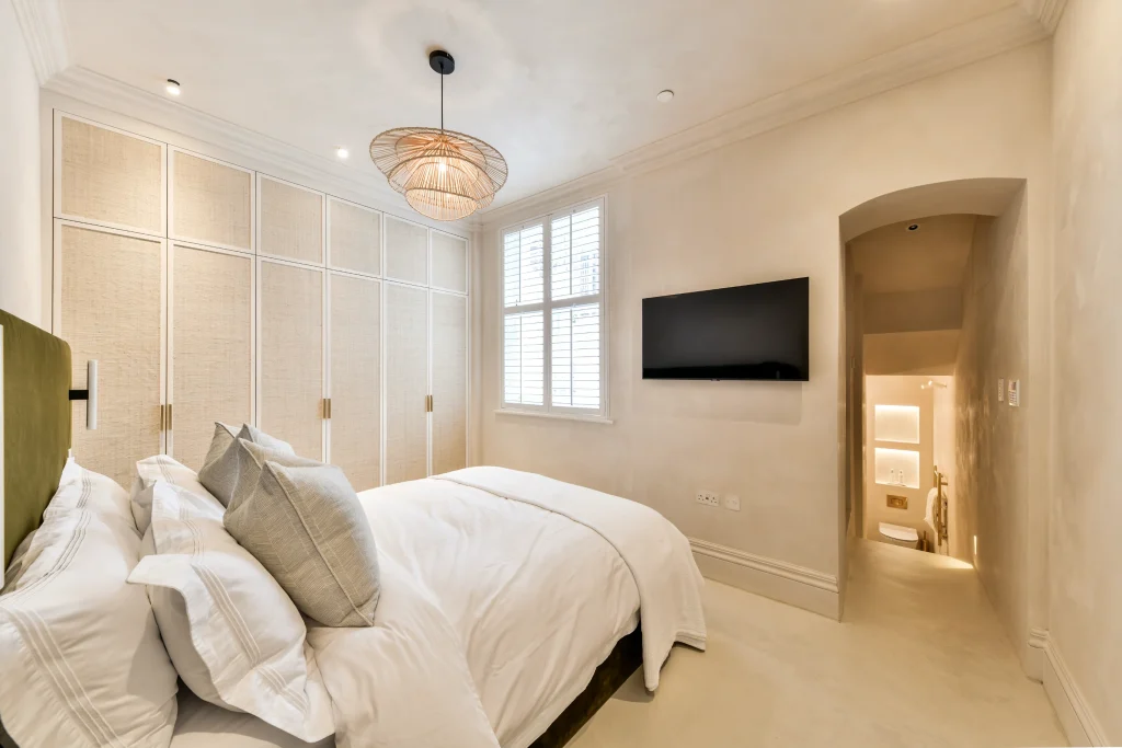 Bespoke master bedroom at Kensington Place with textured walls, raffia storage, and integrated TV