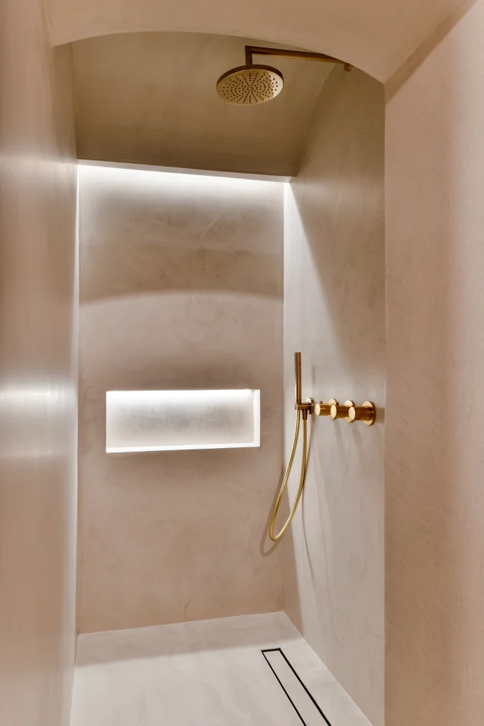 Modern Kensington bathroom: backlit recessed niche, gold brassware, and seamless beige microcement finish