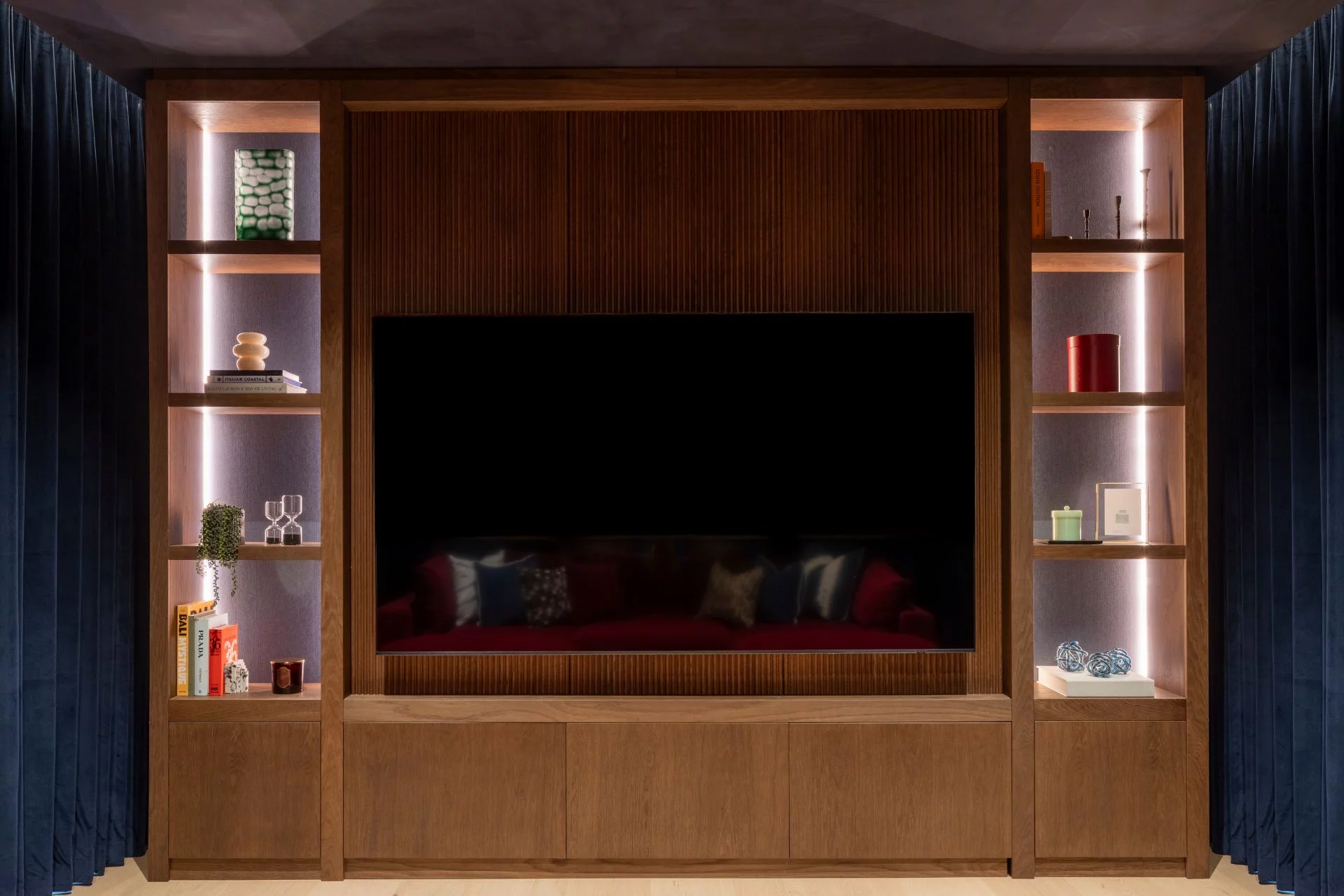 Bespoke walnut media wall for a dedicated cinema room featuring ambient lighting and navy drapes