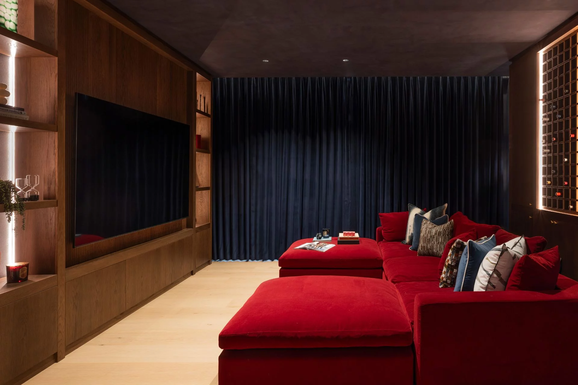 Luxury home cinema with red velvet sectional sofa, fluted wood media wall, and navy curtains by Project London